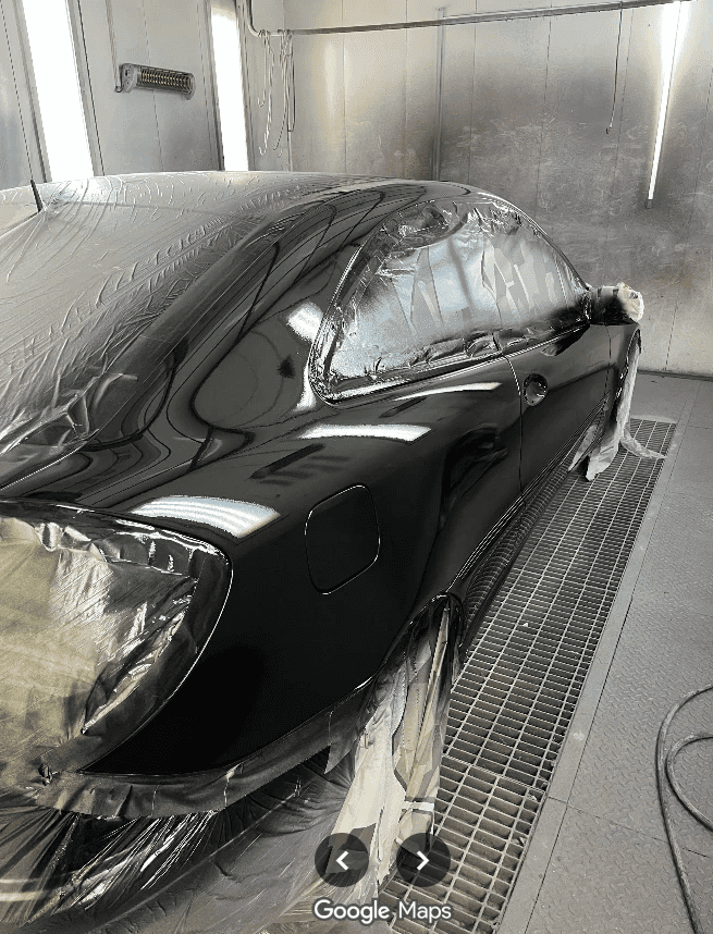 Auto negro enmascarado dentro de la cabina de pintura, con la pintura recién aplicada