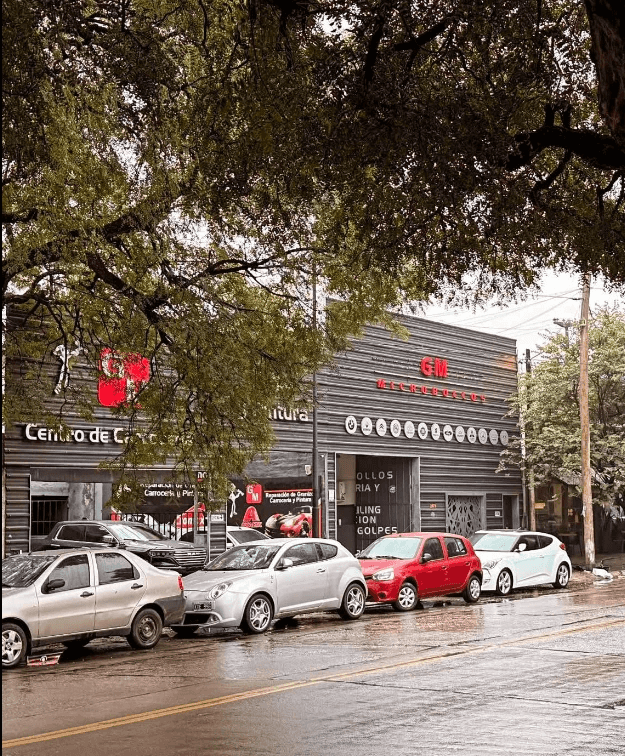 Frente de Taller GM sobre Av. Monseñor Pablo Cabrera, con autos estacionados en un día de lluvia