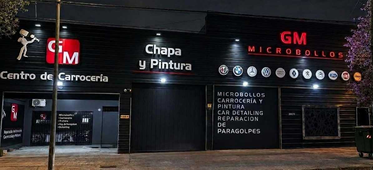 Frente de Taller GM de noche en Av. Monseñor Pablo Cabrera 2873, Córdoba, con los carteles Centro de Carrocería, Chapa y Pintura y GM Microbollos iluminados