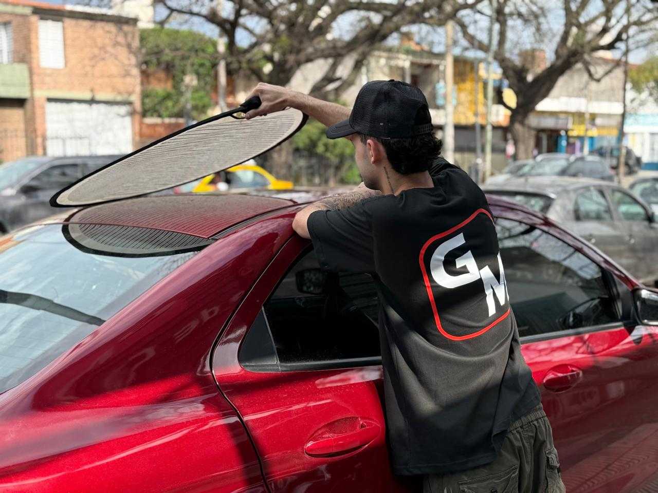Técnico de Taller GM sosteniendo la lámpara de rayas sobre el techo de un auto rojo para ubicar los bollos