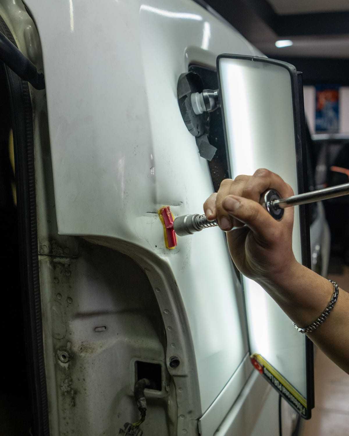 Varilla de microbollos empujando la chapa desde adentro de un panel trasero, con la lámpara de rayas por detrás