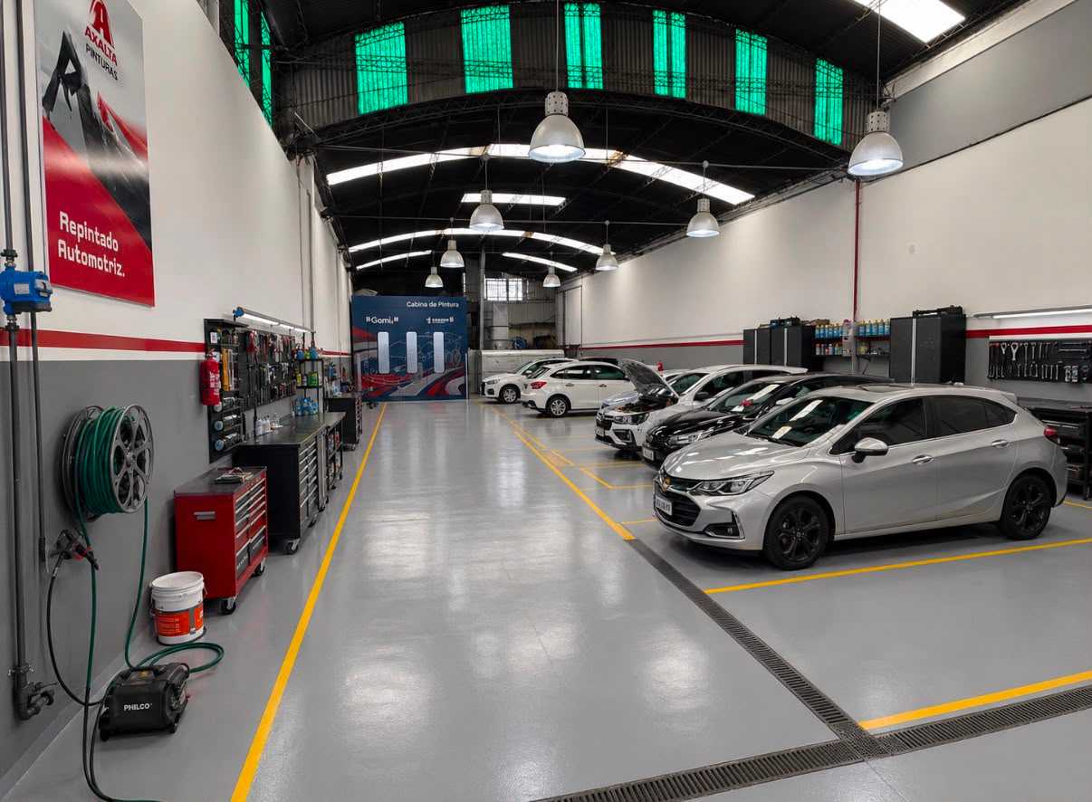 Nave de Taller GM con piso demarcado, autos en reparación y la cabina de pintura al fondo