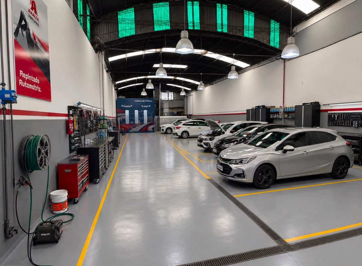 Nave de Taller GM con piso demarcado, autos en reparación y la cabina de pintura al fondo
